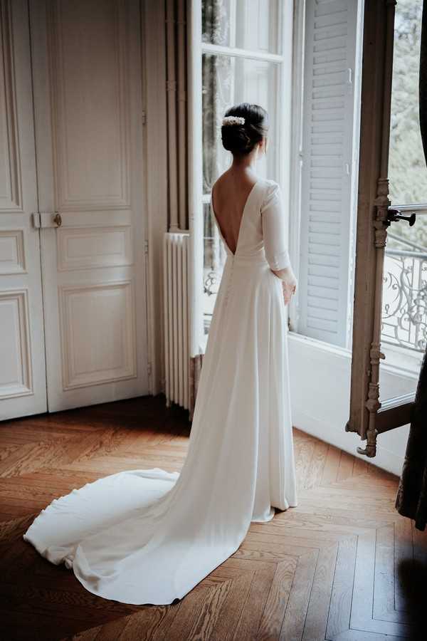 bride looks out french windows in white low back retro wedding dress