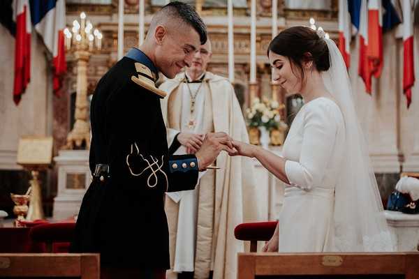 groom places ring on brides finger under watch of the priest