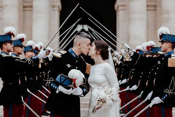 bride in retro wedding dress kisses groom in full military attire at the end of a saber arch