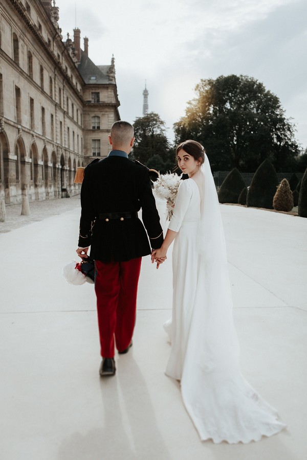 groom in military uniform and bride in low back white retro wedding gown walk away from camera