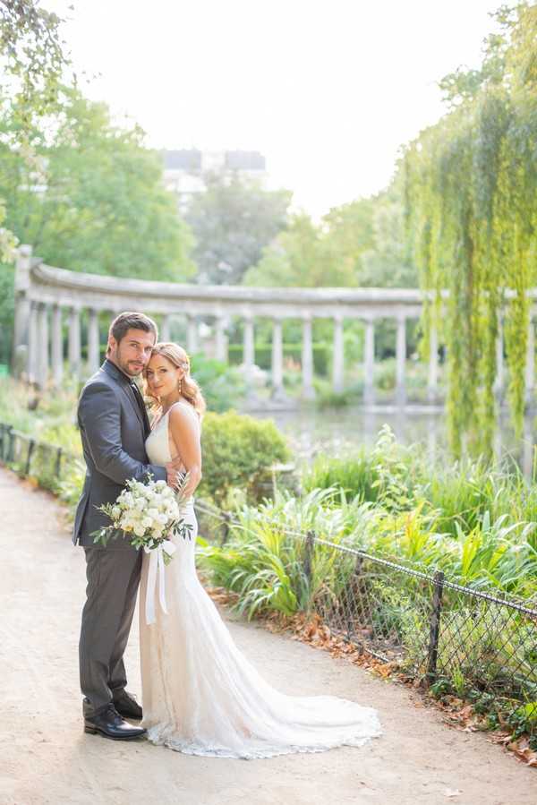 Husband and wife pose in front of lake inside Parc Monceau