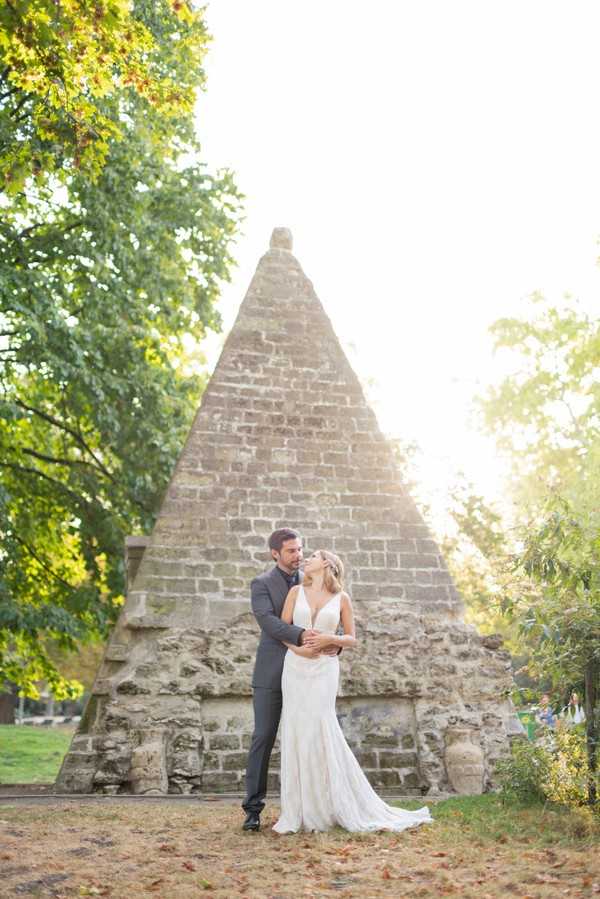 Bride and groom pose in front of miniature egyptian pyramid in Parc Monceau in Paris