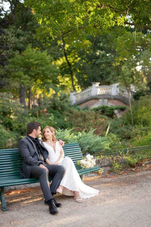 Bride and groom seated on green park bench