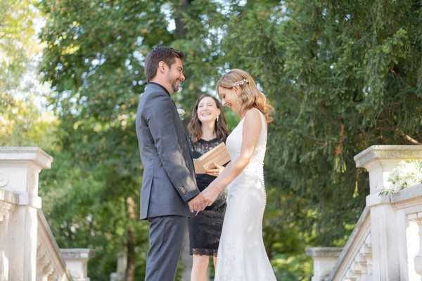 Bride smiles broadly while taking her husband hands in front of officiant