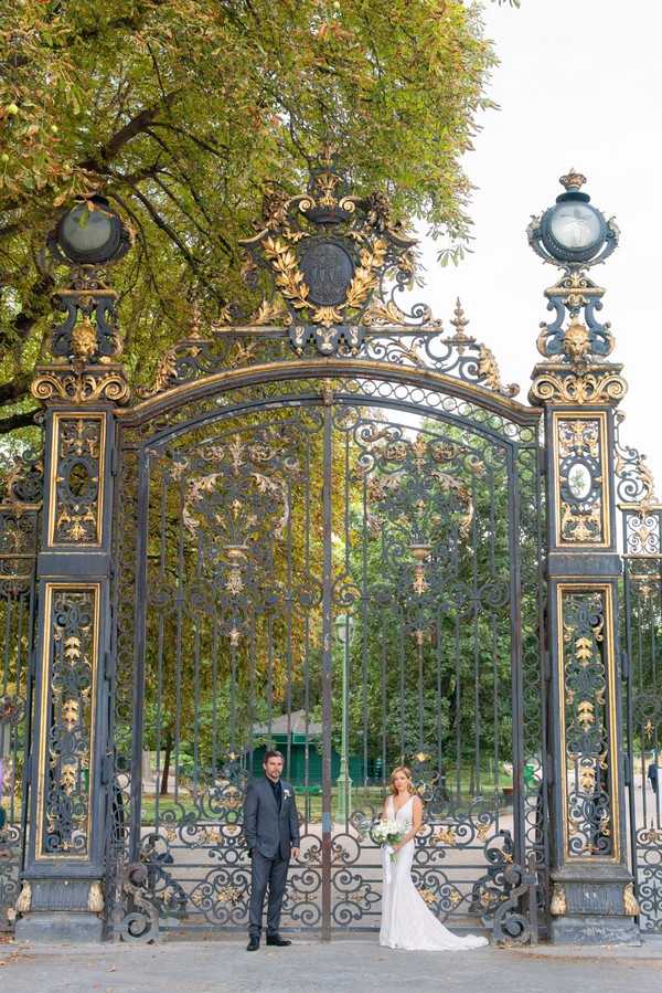 bride and groom stand in front of black and gold wrought iron gates