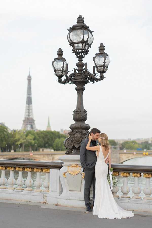 bride and groom close eyes and kiss in front of view of the Eiffel Tower