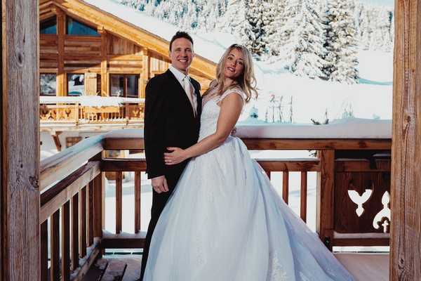 bride and groom posing on the balcony of a private chalet in french alps with snow and trees visible in the background