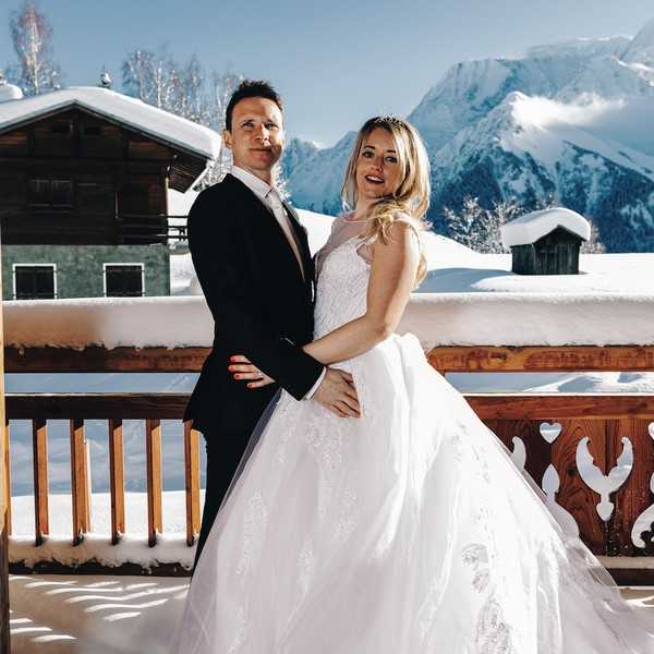 bride and groom in front of snowy backdrop of mountains, trees and chalets