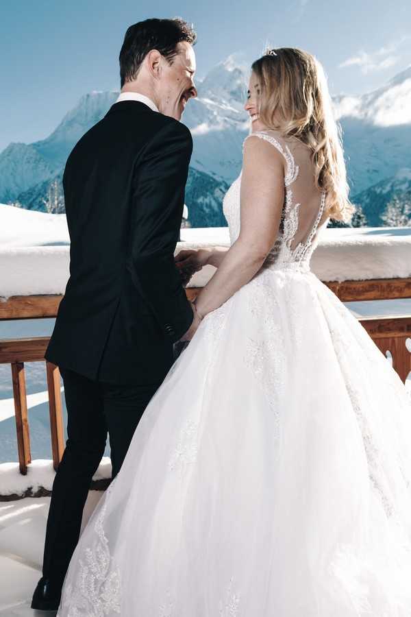 bride and groom laugh and turn back to camera, a snowy mountain is visible in the backfground