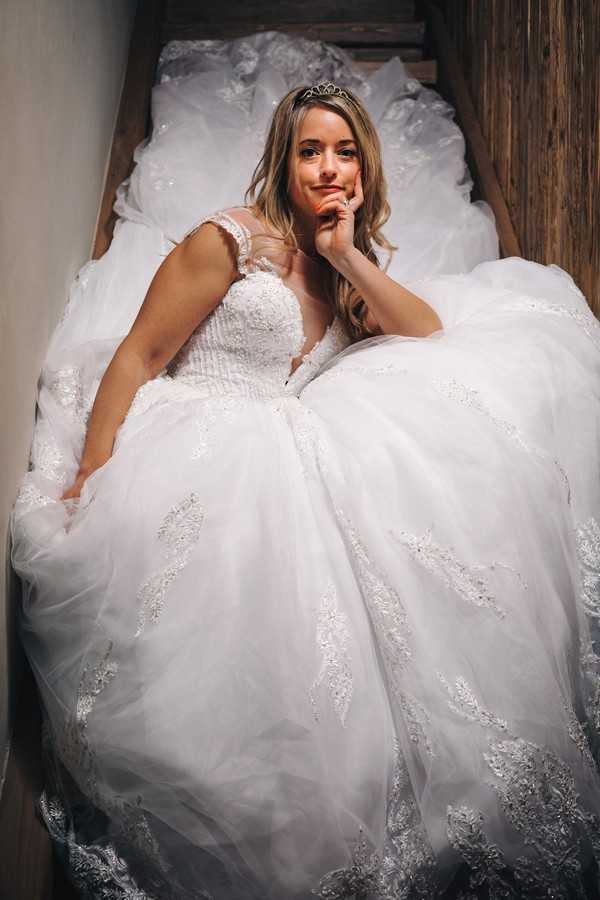 bride sits in stair well surrounded by her voluminous wedding skirt