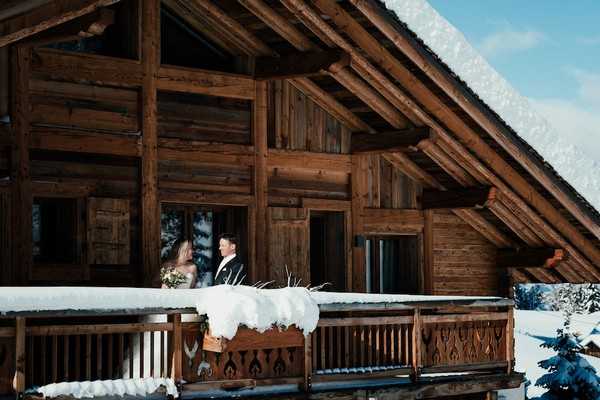 Bride and groom on the balcony of a wooden private chalet for their magical alpine village wedding in the French Alps