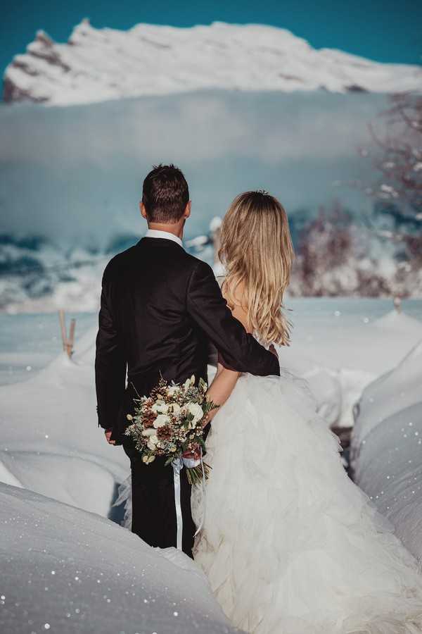 bride and groom have backs turned to camera and are completely surrounded by sparkling snow and french snowy alps