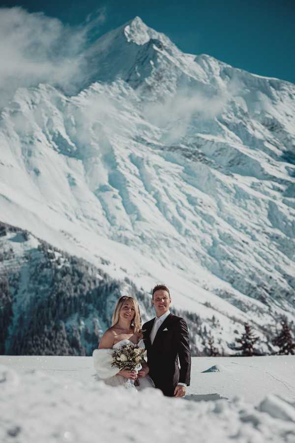 bride and groom smile in front of stunning scenery of snow covered french alps