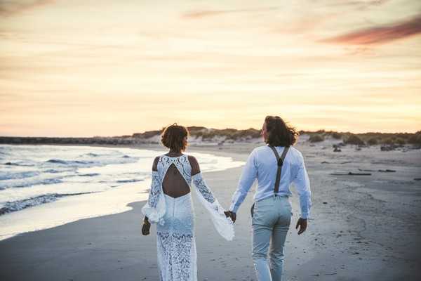 Couple walk hand in hand with back to camera on beach at sunset