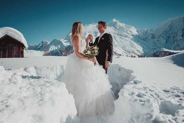 groom takes his brides hand waist high in the white snow with the french alps in the background