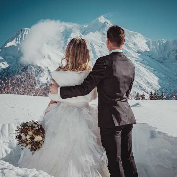 groom has his arm around his bride as they look up at the snowy mountains in the distance. 