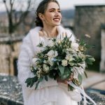 Bride in fur coat with bouquet smiles into distance