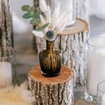 Log used as small table for brown vase of flowers at wedding reception