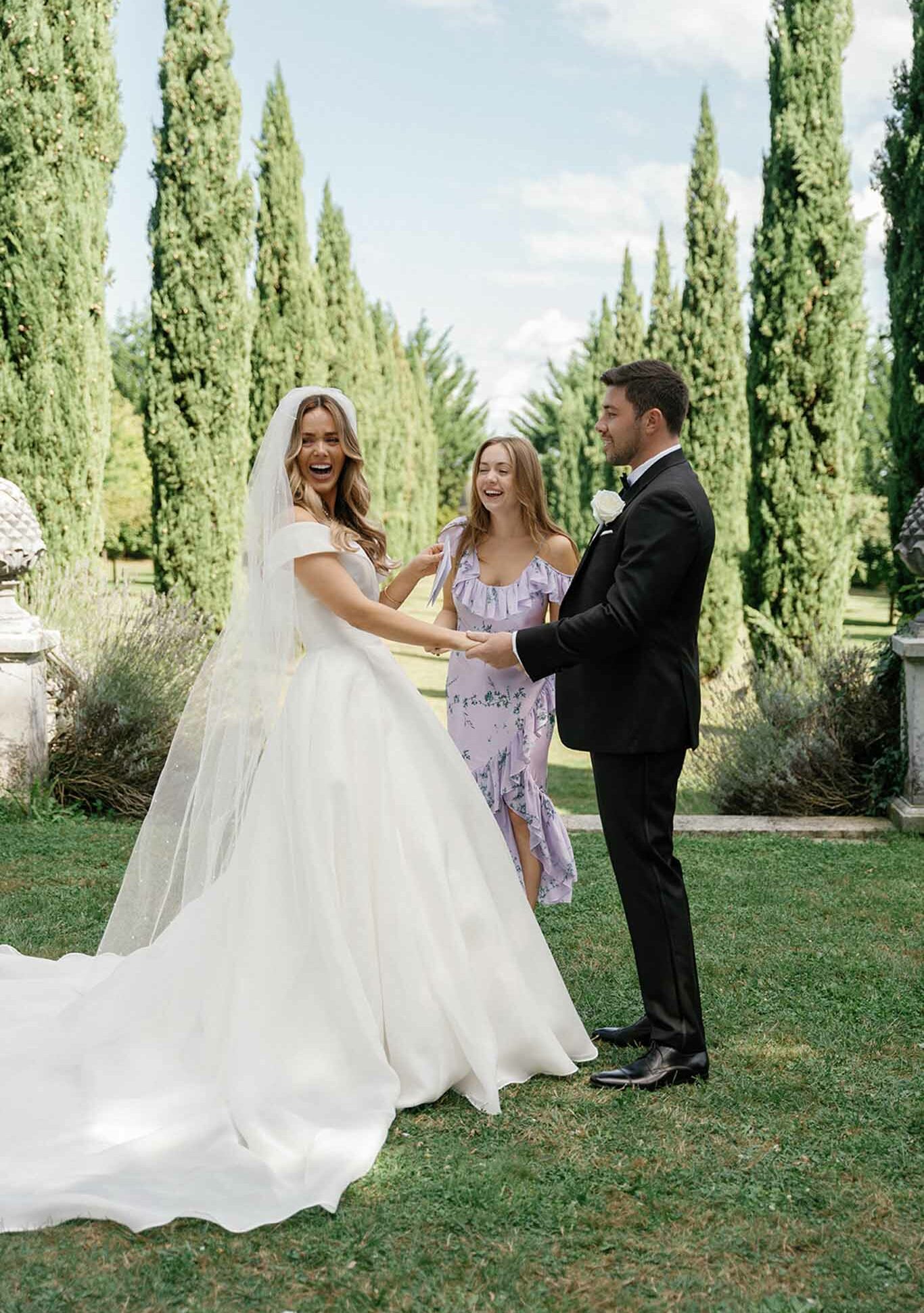 Bride and groom exchanging vows during outdoor ceremony in formal garden with cypress trees