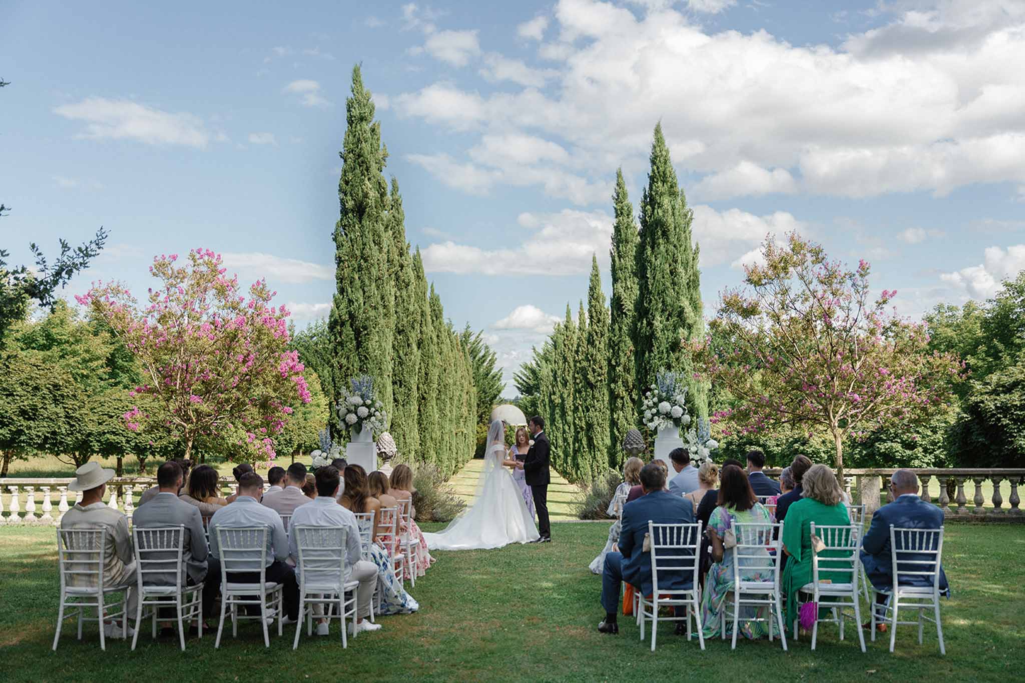 Outdoor wedding ceremony with white arch and cypress trees in formal garden estate setting