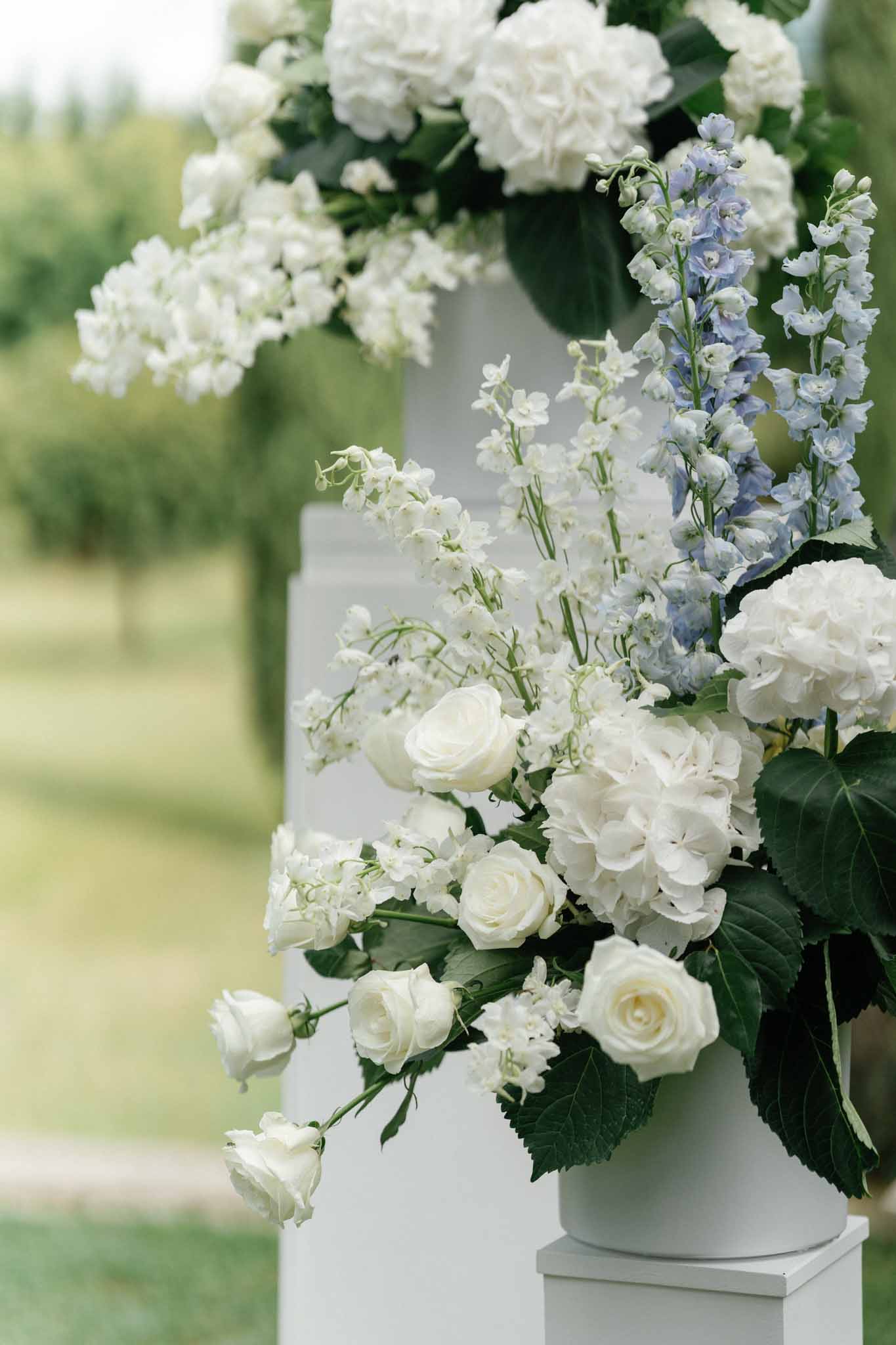 White and blue wedding floral arrangement in pedestal vase at outdoor garden venue