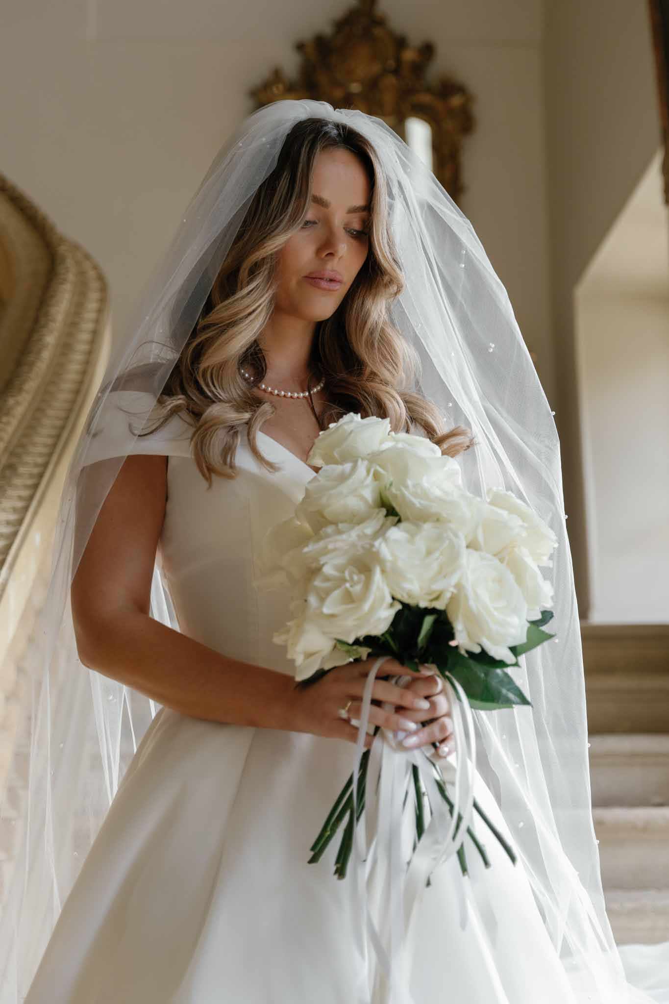 Bride in ivory wedding dress with bouquet in elegant interior with gold mirrors
