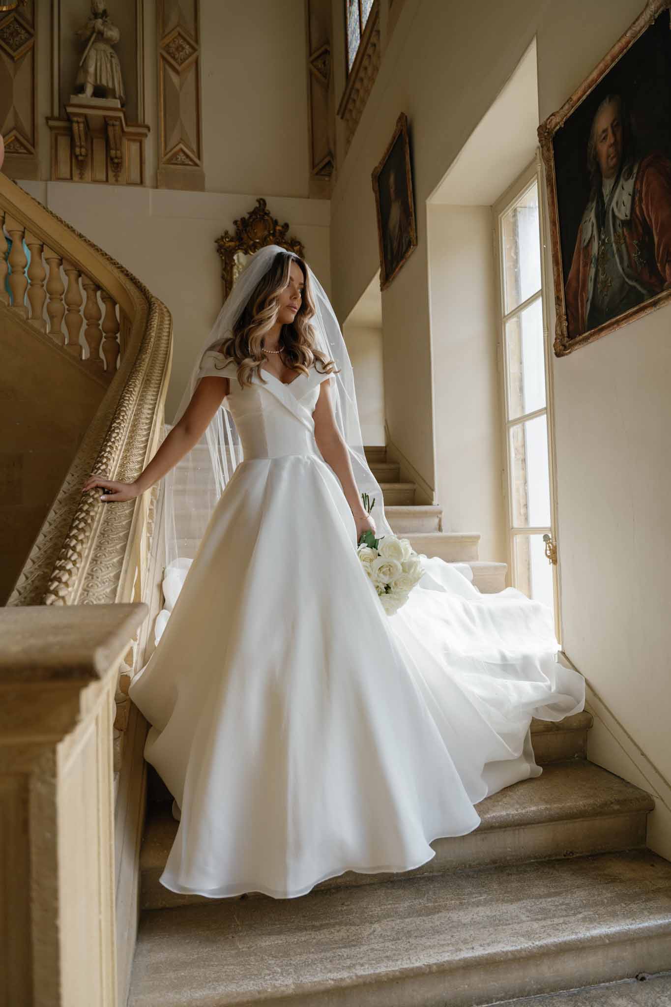 Bride in ivory ball gown descending grand staircase in classical interior with gilt details and natural light