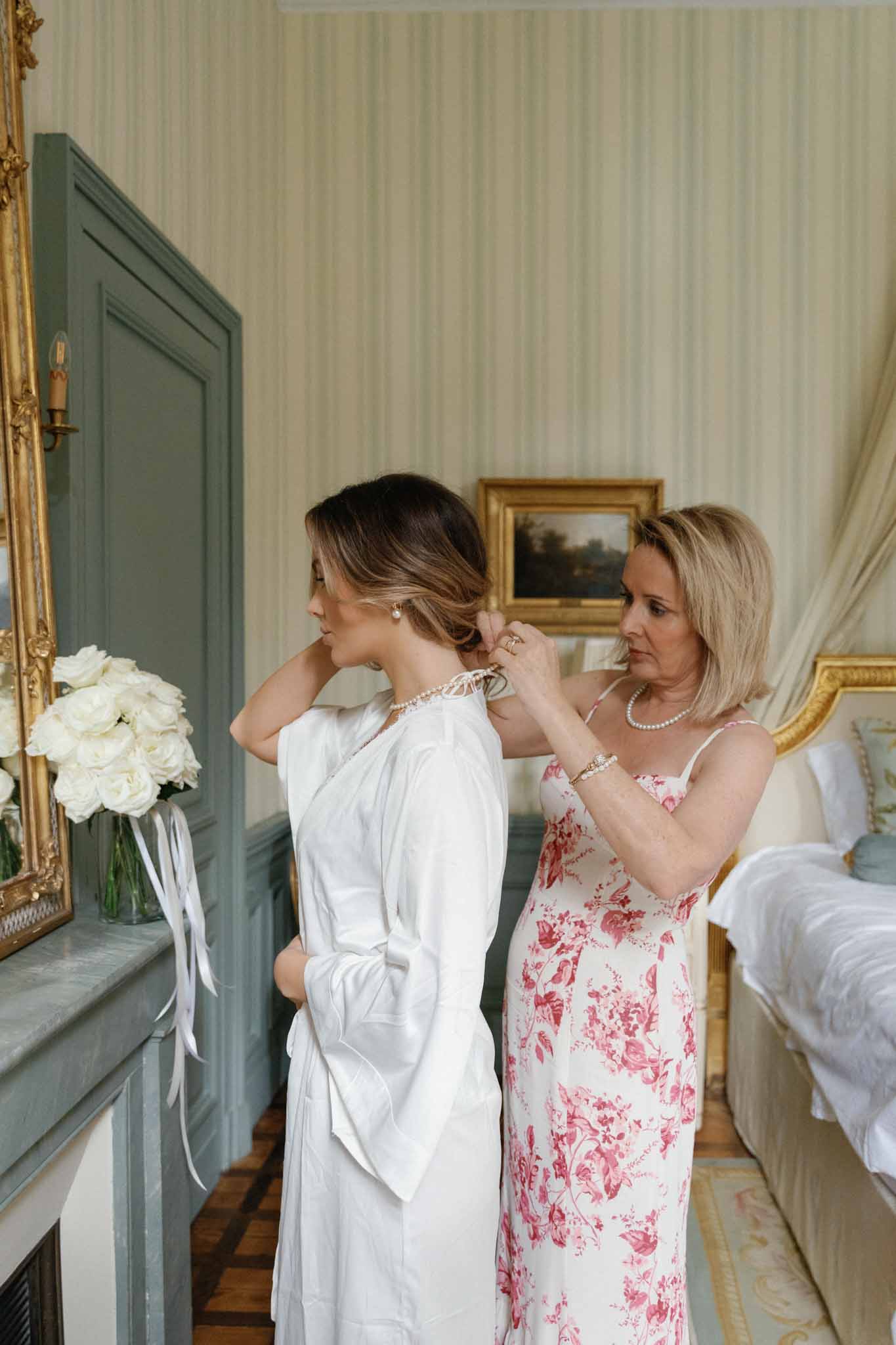 Bride being helped with pearl necklace during getting ready in elegant interior room