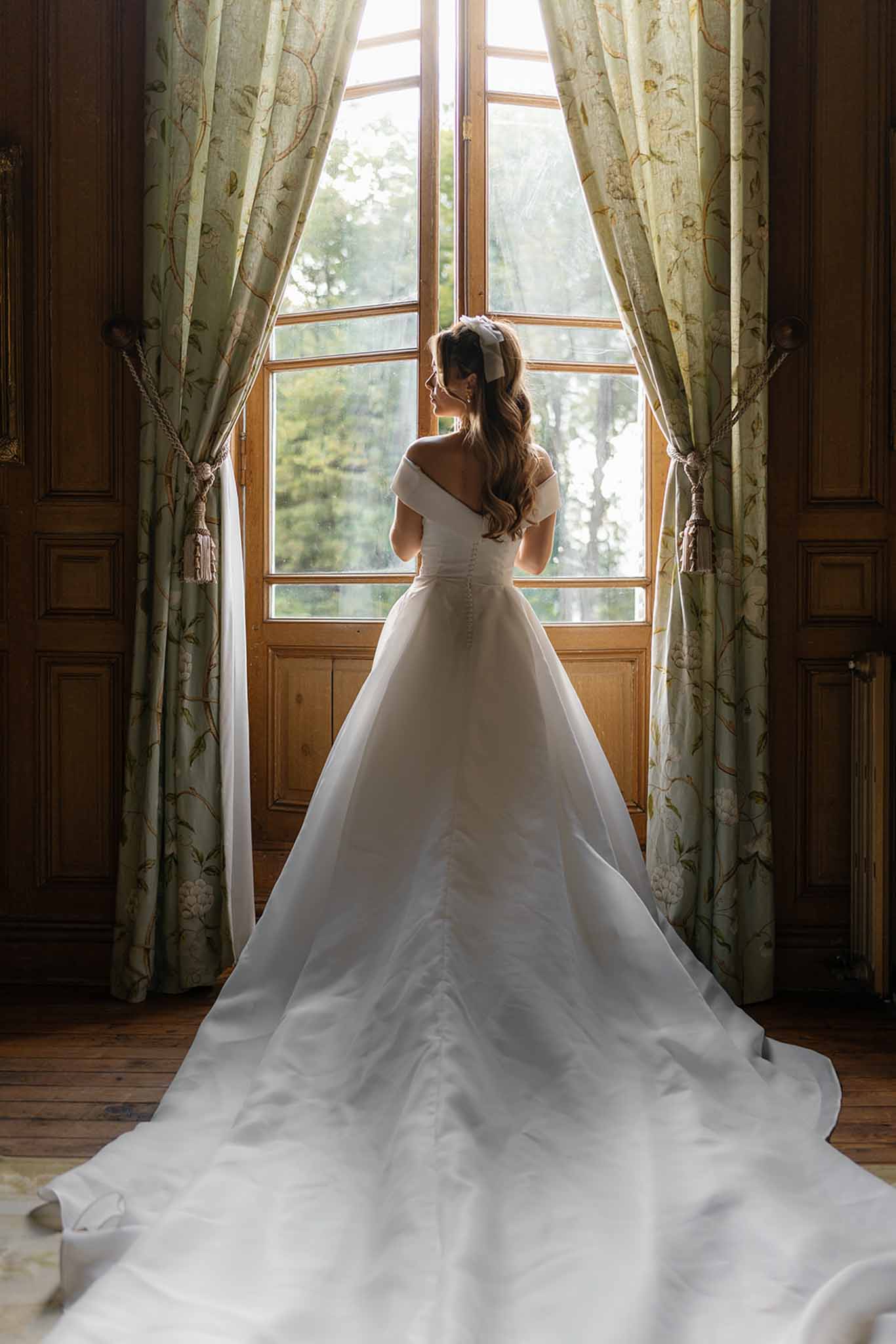Bride in ivory gown standing by window in historic interior space