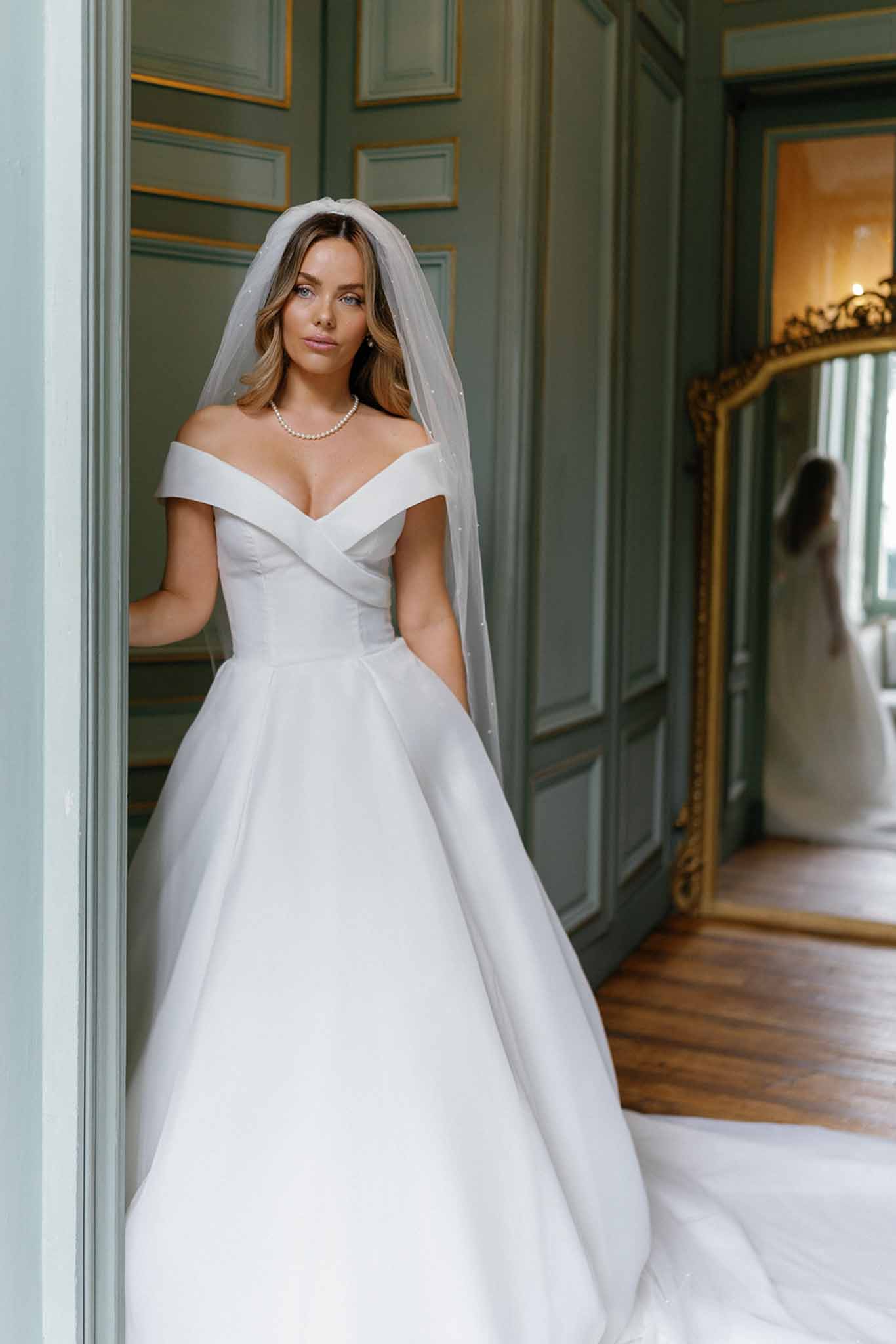 Bride in ivory wedding dress and veil standing in classical interior hallway with sage green doors