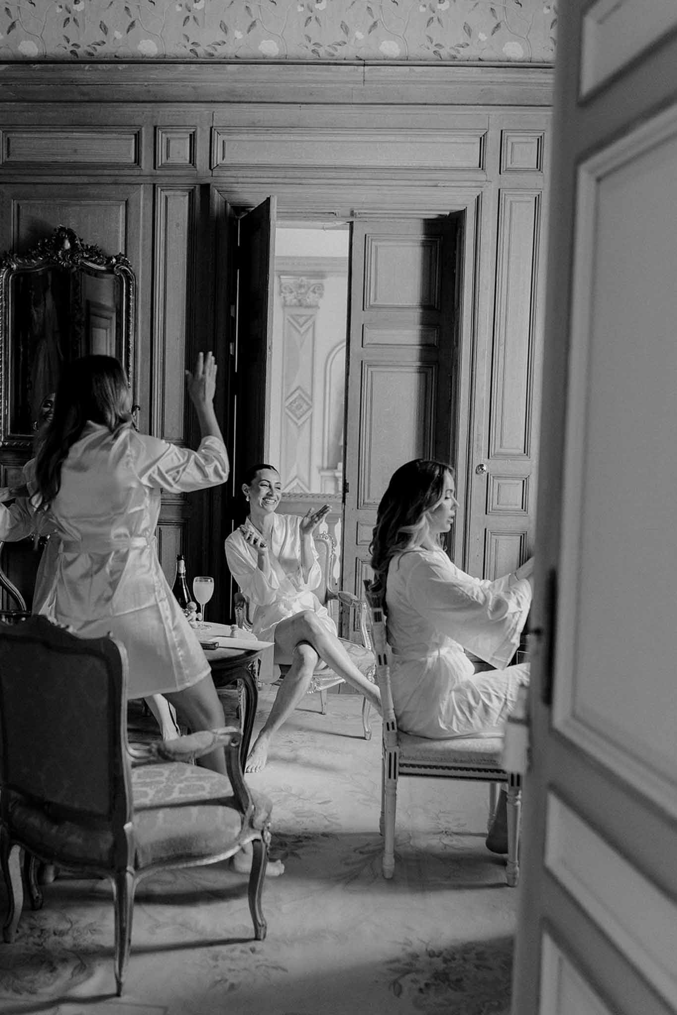 Three women in robes preparing for wedding in classic French chÃƒÂ¢teau interior with paneled walls