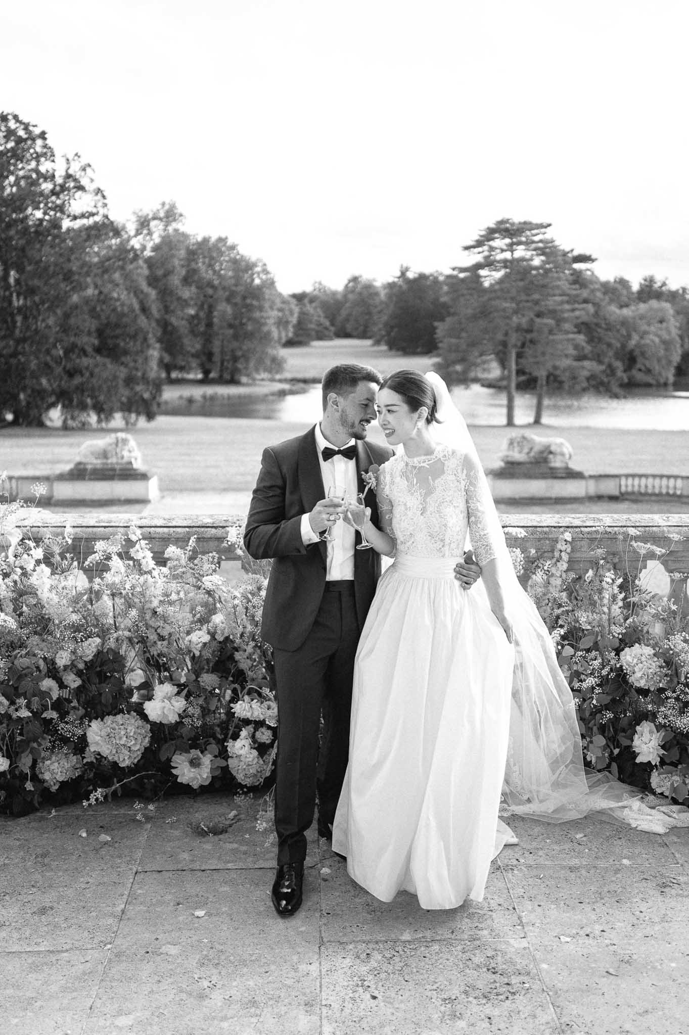 Black and white bride and groom on terrace balustrade with formal garden canal and tree allee behind