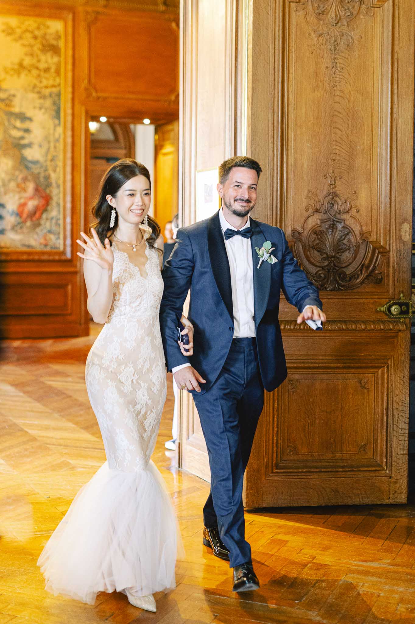 Couple making grand entrance through carved doors into chateau reception bride in lace gown groom in navy tuxedo