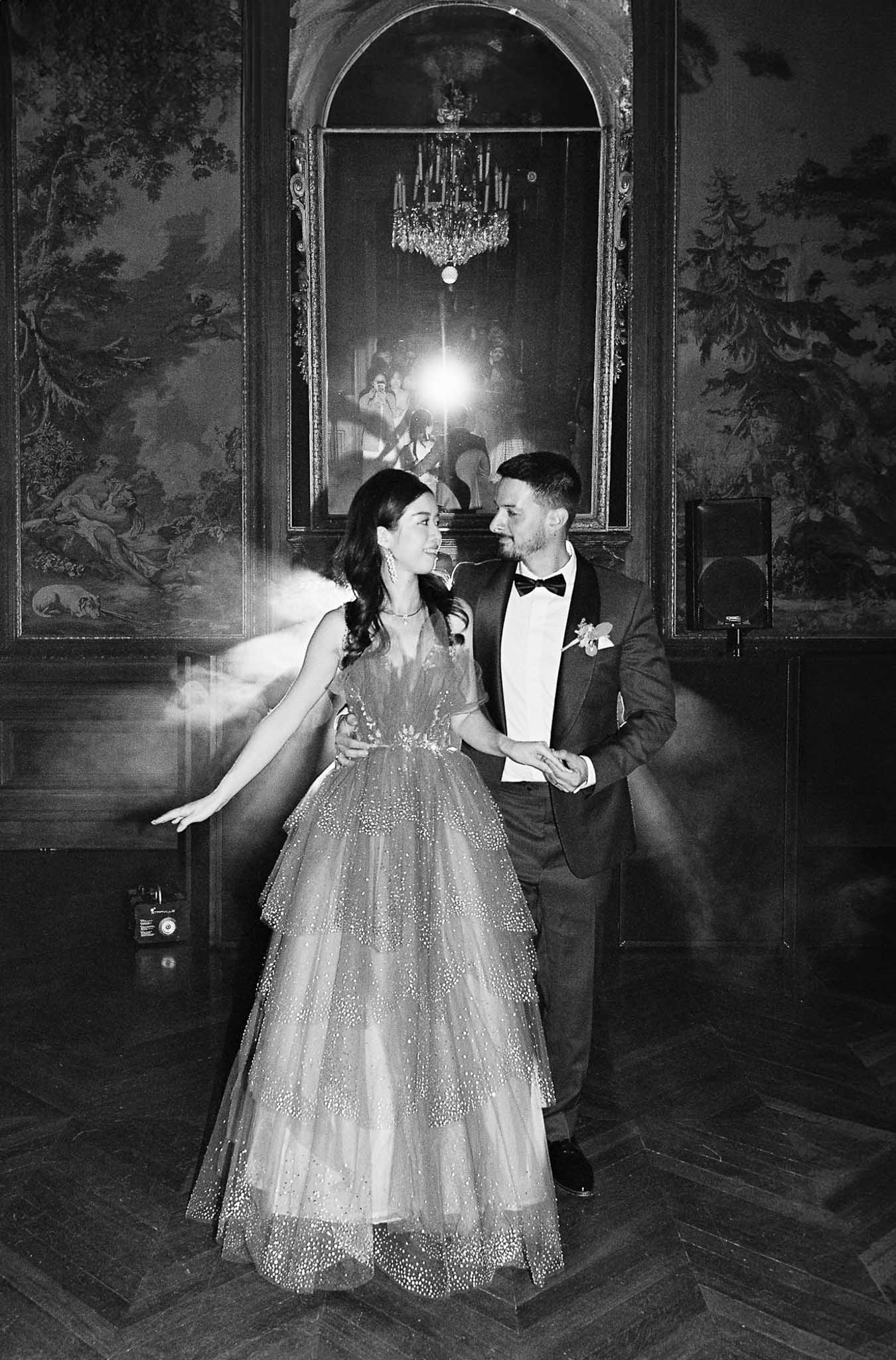 Black and white film portrait of couple dancing in ornate ballroom with gilt mirror and flash