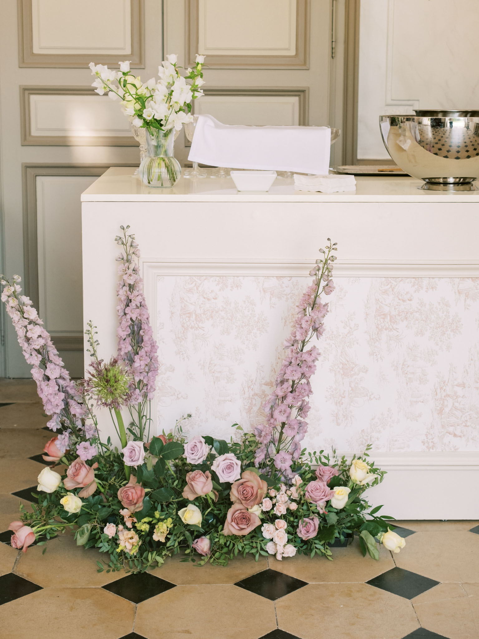 Toile-panelled bar with ground-level installation of mauve roses, blush blooms, and lavender delphiniums