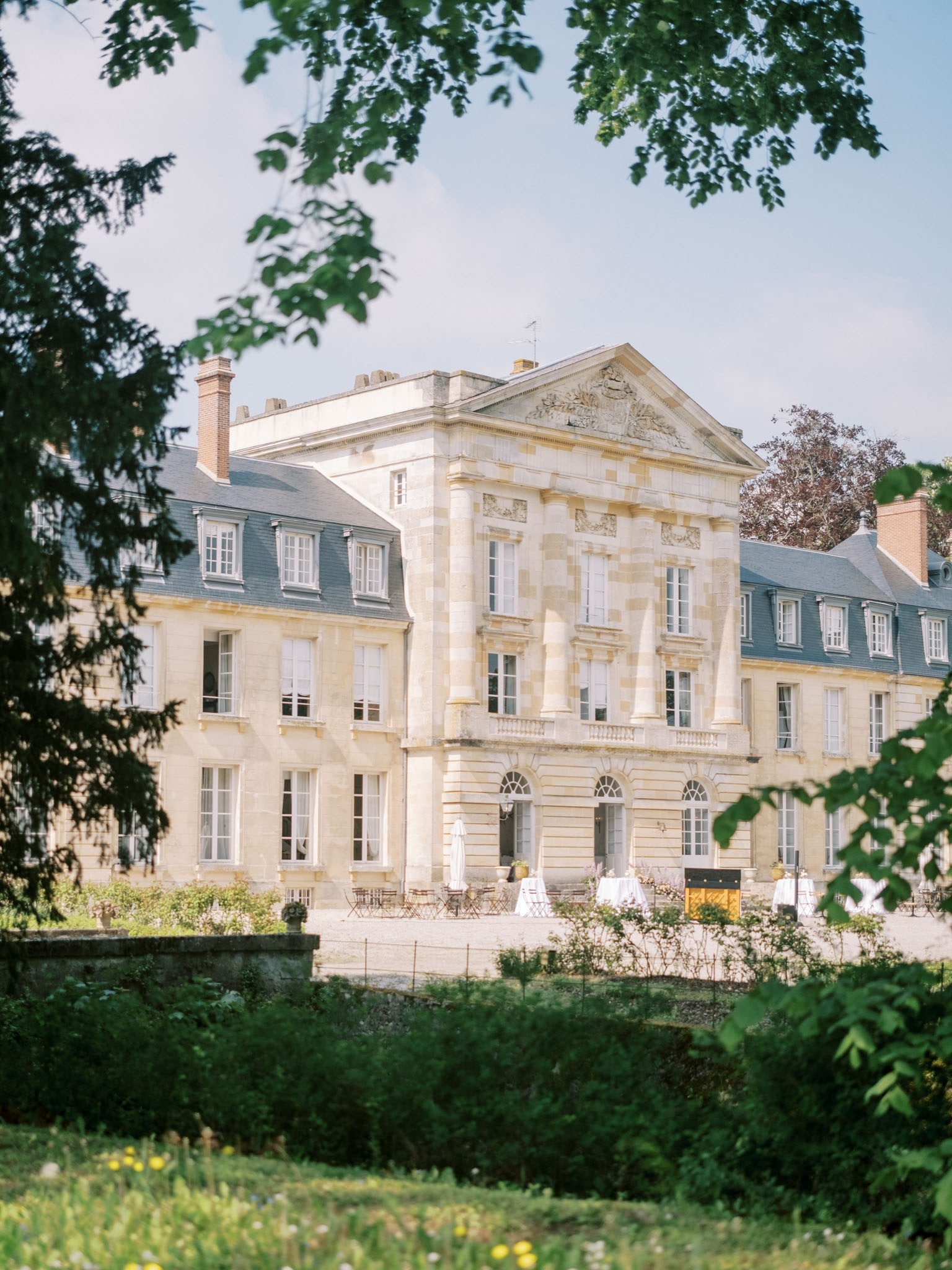 Three-storey cream stone French chateau with slate mansard roof and terrace set with white-clothed reception tables