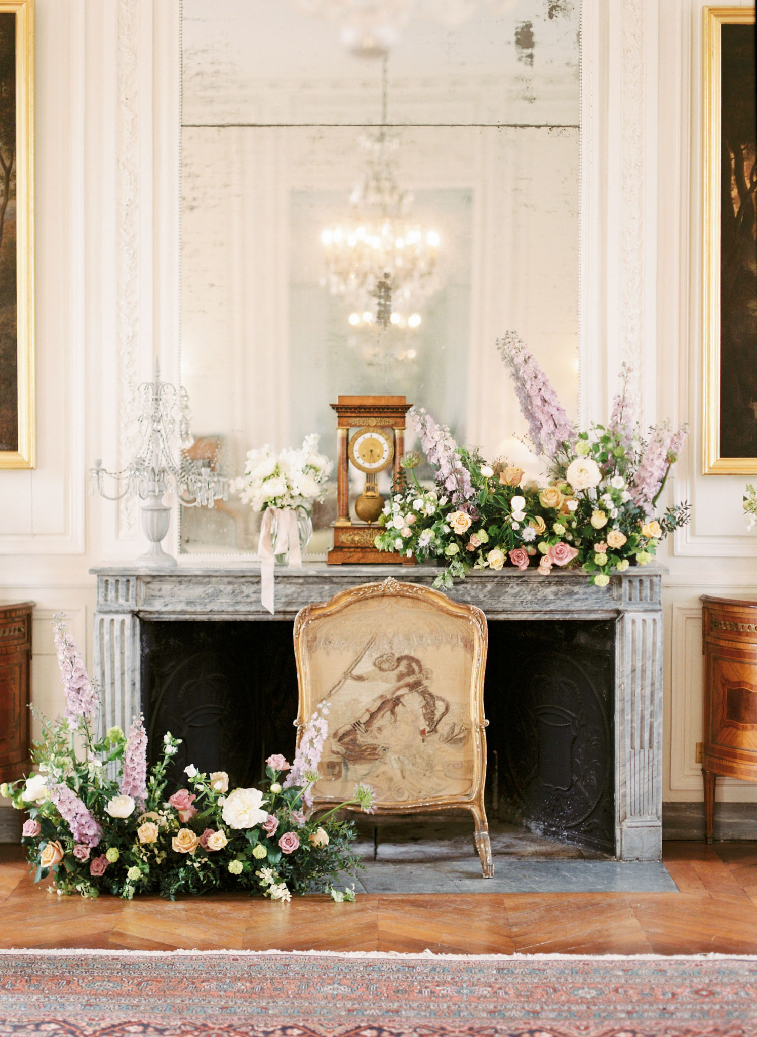Chateau salon fireplace with mauve rose peach spray and lavender delphinium arrangements gilt clock boiserie and chandelier