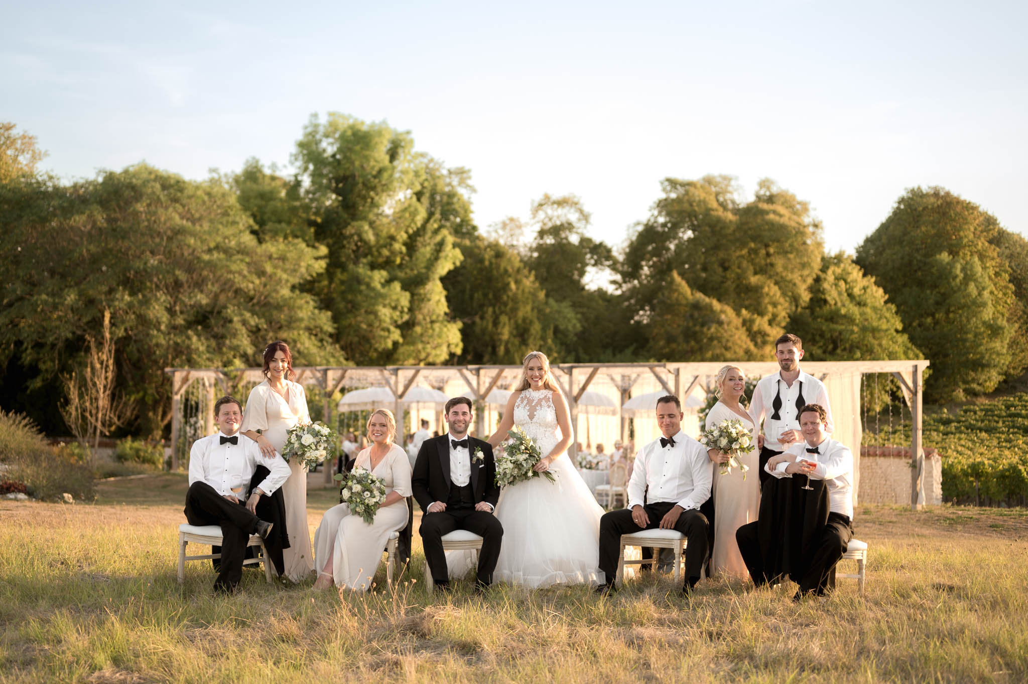 Bridal party of ten posed in garden with bridesmaids in champagne gowns and groomsmen in black tuxedos