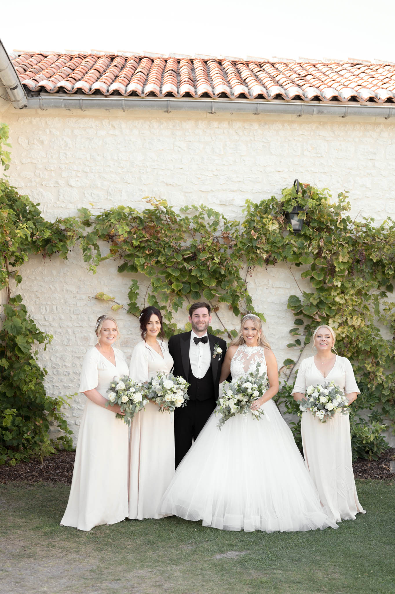 Bride groom and two bridesmaids in blush chiffon with white rose bouquets at stone building