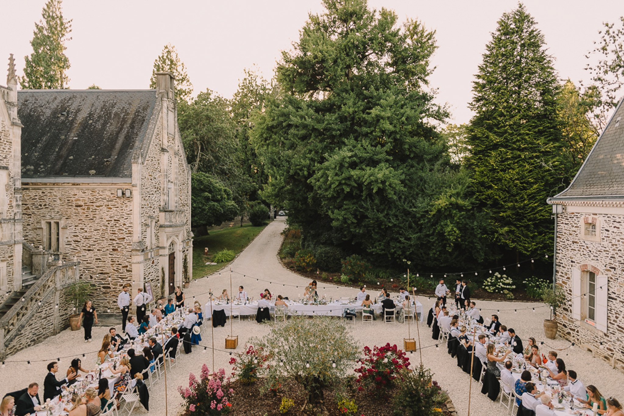 Aerial view of U-shaped reception tables for 100 guests with festoon lights in chateau courtyard at dusk