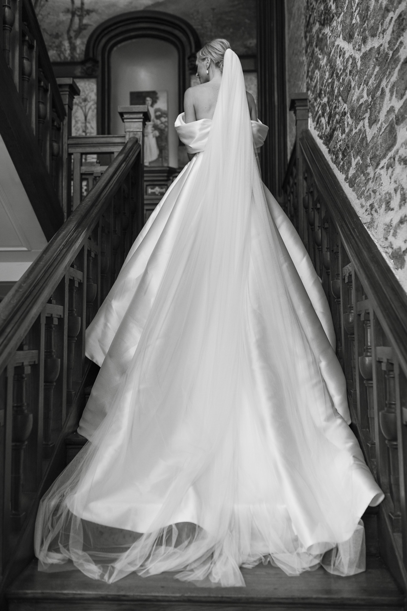 Black-and-white portrait of bride from behind on a wooden staircase with cathedral train cascading down the steps