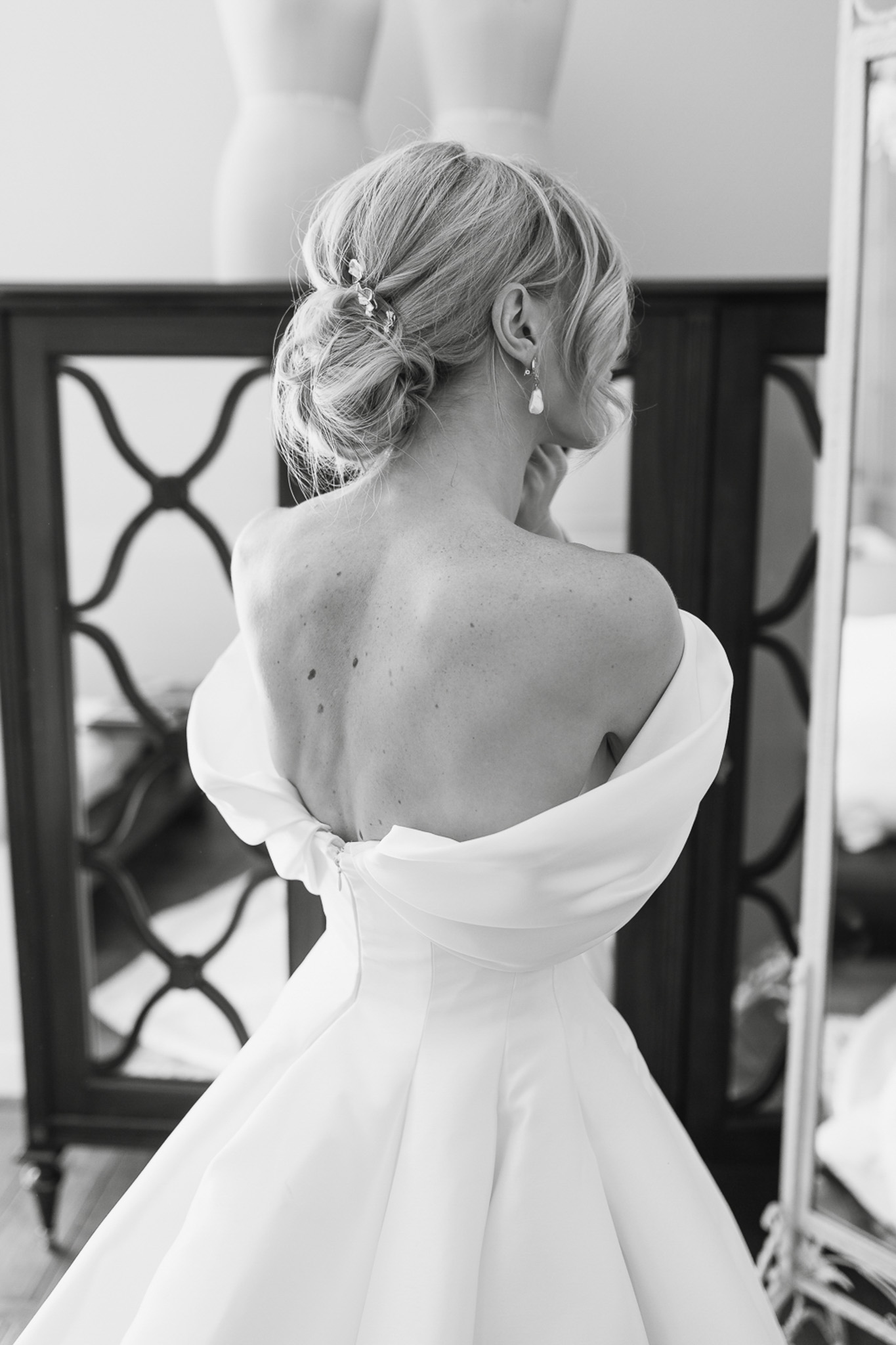 Black-and-white portrait of bride from behind showing off-the-shoulder gown with bow detail and low updo