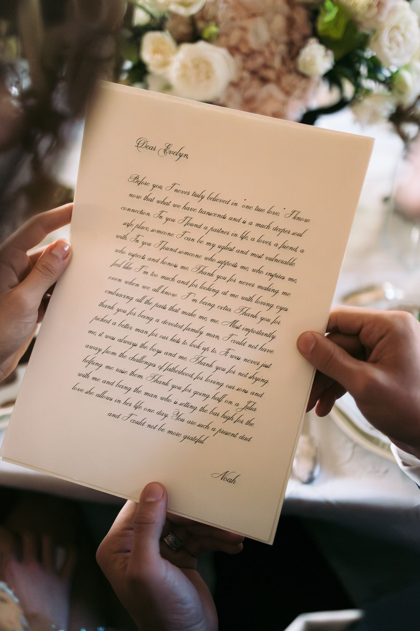Handwritten wedding vow letter in black calligraphy on cream paper held open by two hands