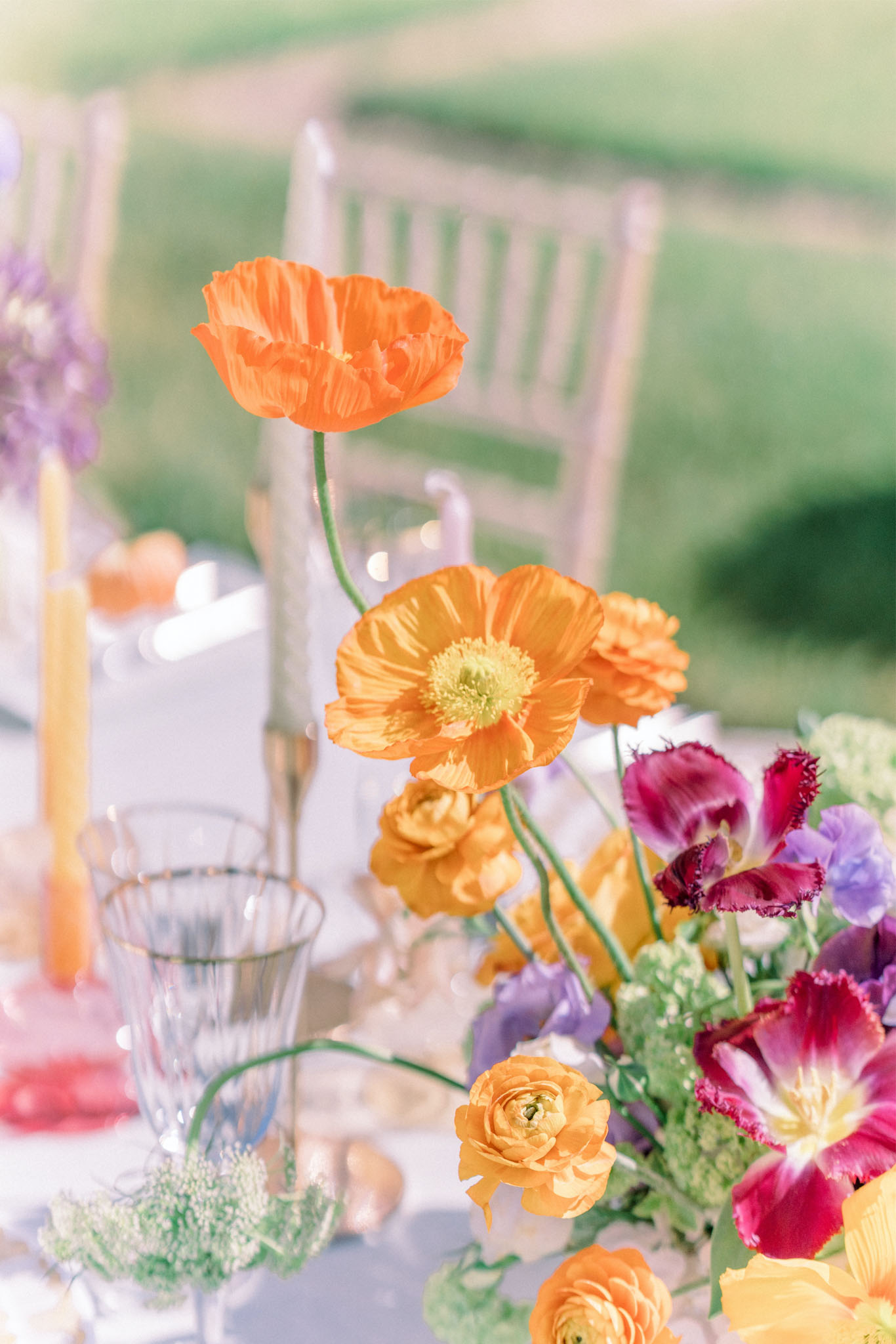 Jewel-toned centerpiece with orange poppies magenta tulips lavender sweet peas and yellow taper candles