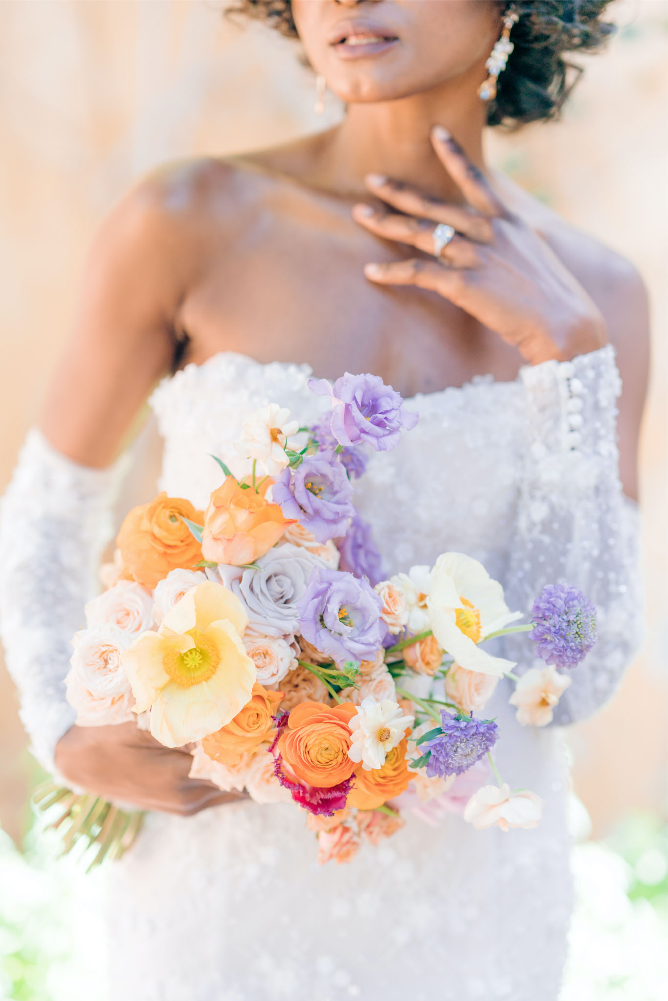 Close-up of bride holding garden-style bouquet of orange ranunculus, lavender lisianthus, and cream poppies
