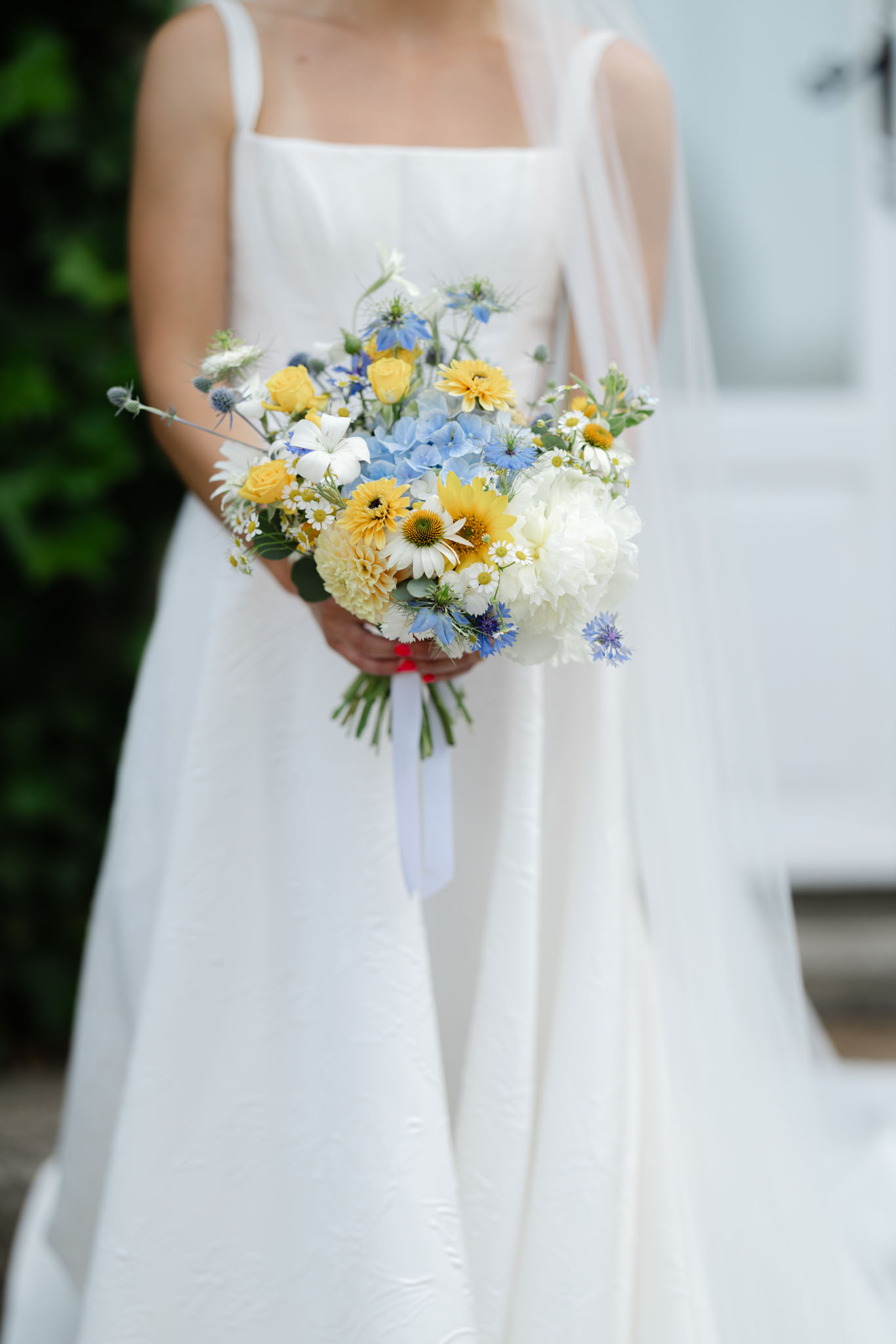Close-up of bride holding wildflower bouquet of yellow roses, blue cornflowers, and white peonies