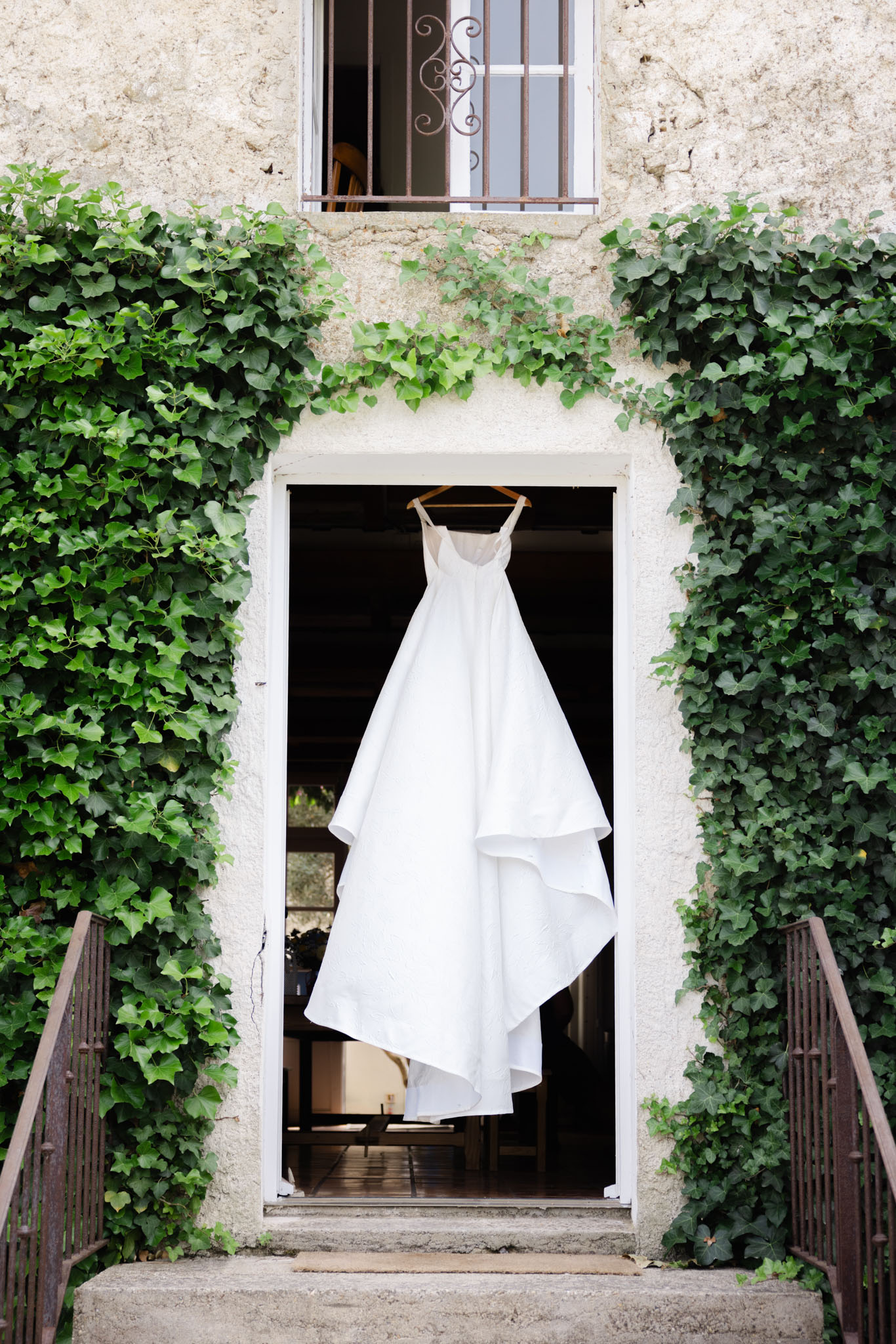 White tiered wedding dress on wooden hanger in ivy-framed stone doorway of French chateau