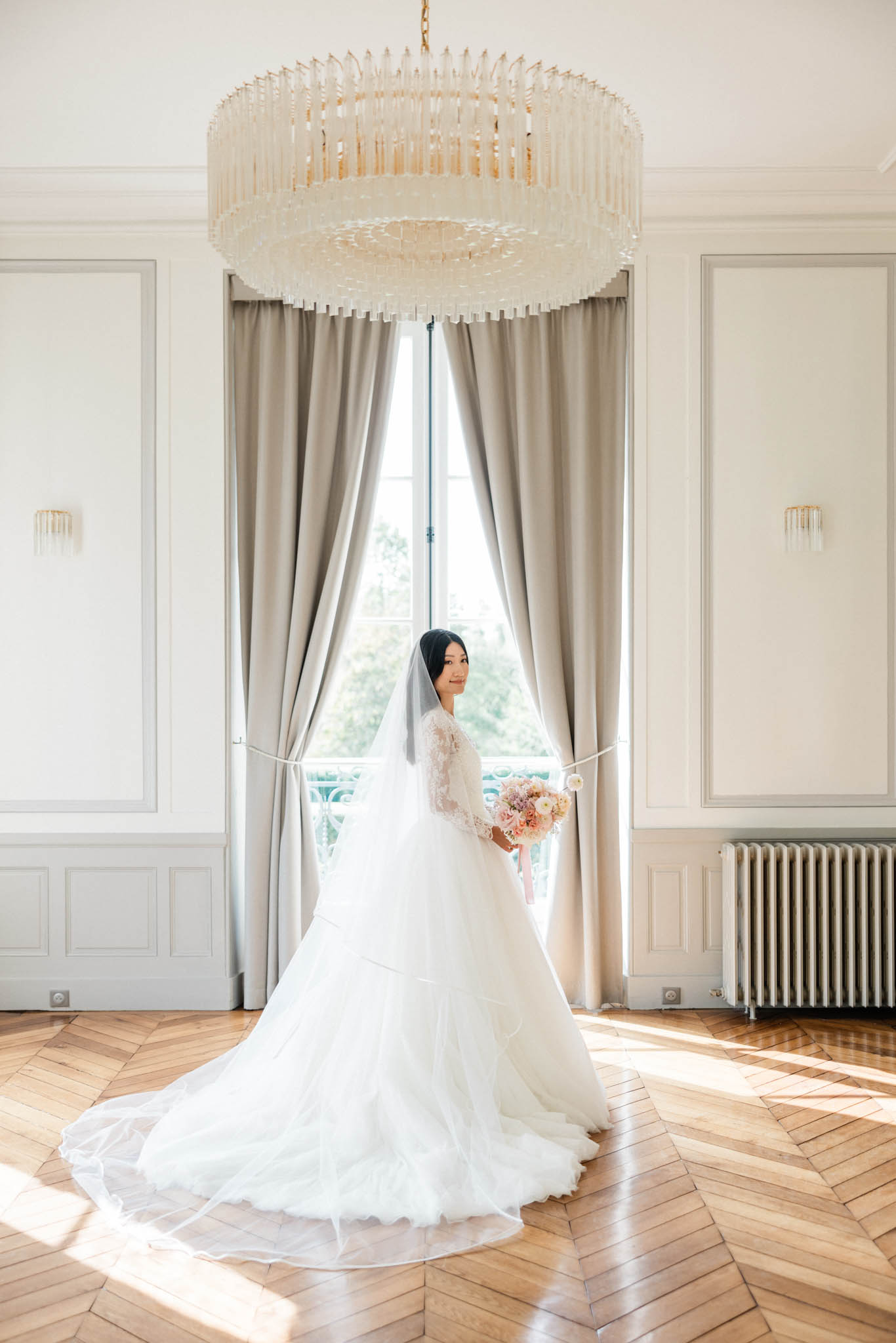 Bride in lace long-sleeve ball gown and cathedral veil holding peach and blush bouquet in French panelled room
