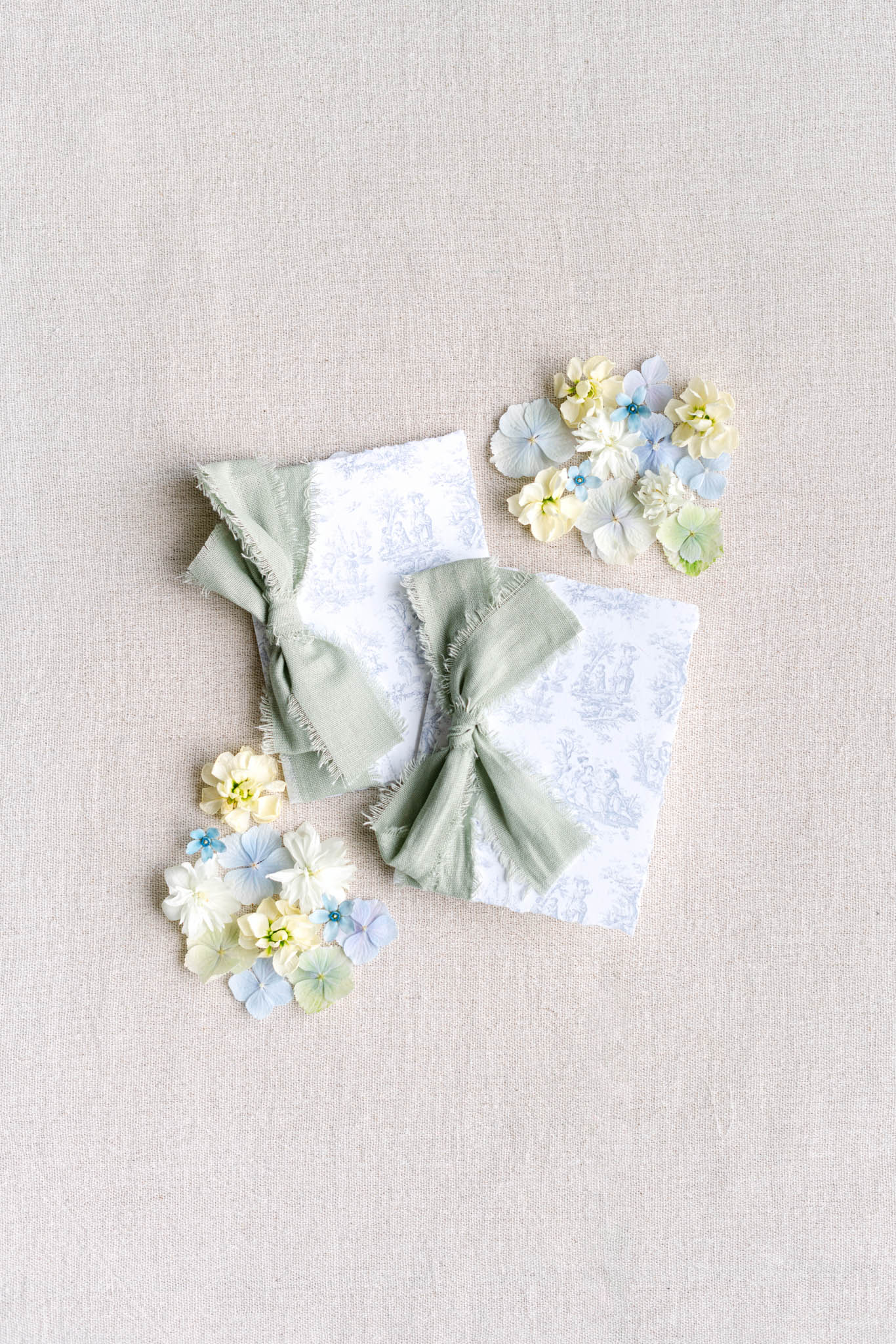 Flat lay of blue toile de Jouy wedding stationery tied with sage ribbon surrounded by small flowers
