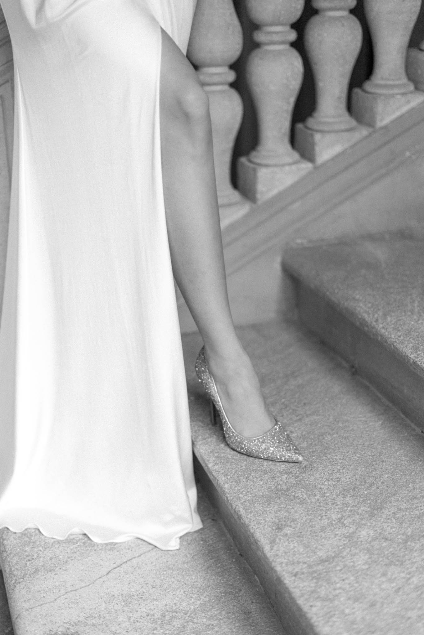 Bride's pointed-toe glitter stiletto on stone staircase with flowing white gown, black and white photo